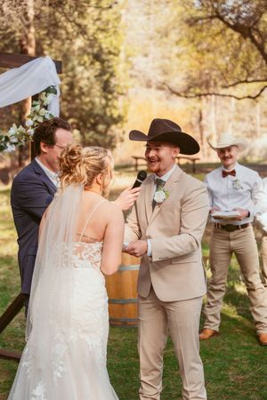 A rustic outdoor wedding ceremony with attendees gathered under tall pine trees.