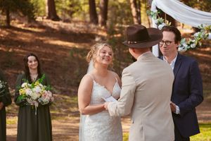Outdoor forest wedding ceremony with decorated wooden arch and pine trees in background.