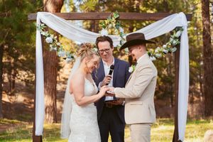 Outdoor wedding ceremony under a white draped arch in a serene forest setting.