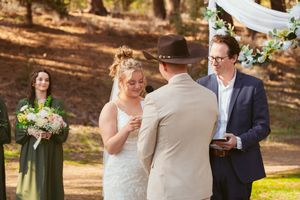 Wedding couple exchanges vows during outdoor forest ceremony with officiant and bridesmaid in sage dress.