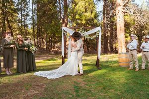 Wedding ceremony under white fabric arch with bridesmaids in forest setting.