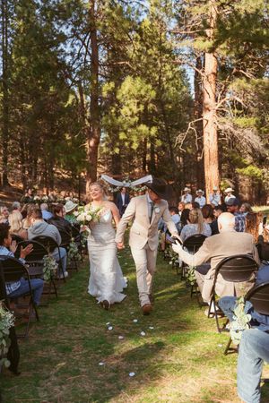 A couple celebrates their wedding ceremony in a beautiful forest setting surrounded by guests seated on folding chairs.