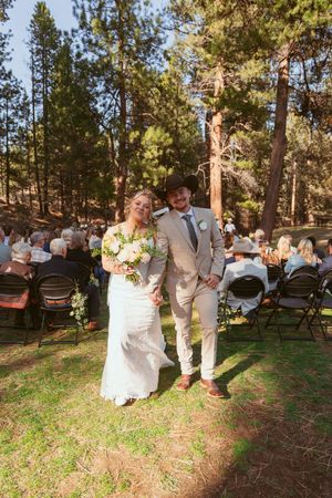 Wedding ceremony exit at an outdoor forest venue with wooden chairs and floral decorations.
