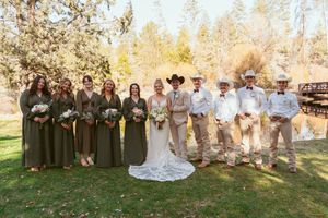 Wedding party poses outdoors in brown and white attire with cowboy hats against autumn foliage.