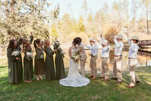 Wedding party in olive green dresses and khaki attire pose outdoors in autumn with rustic wooden fence backdrop.
