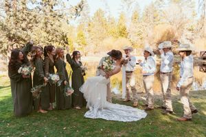 Bridal party with attendants in dark gowns and light suits pose playfully outdoors during autumn wedding celebration.