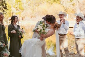 A romantic outdoor wedding ceremony takes place by a pond on a sunny autumn day with guests in western attire.