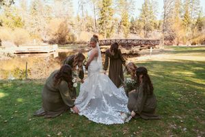 Group helps arrange the delicate lace train of a wedding dress outdoors against an autumn backdrop.