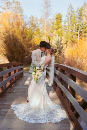 A wedding couple sharing an intimate moment on a wooden bridge surrounded by autumn foliage.
