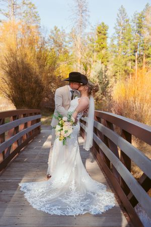 Romantic wedding portrait on a wooden bridge surrounded by autumn foliage and evergreen trees.