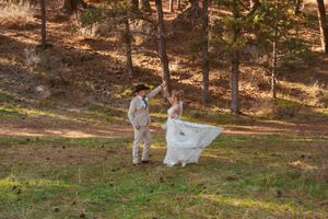 A couple twirls playfully in a sunlit forest clearing during their wedding photoshoot.