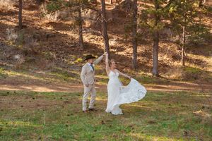 A couple dances and spins in a scenic wooded area on their wedding day.