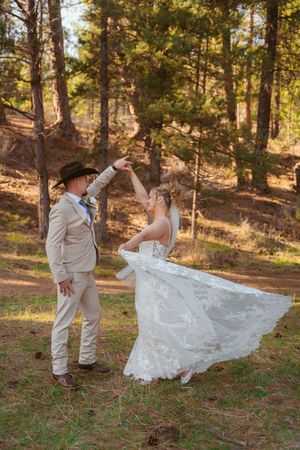 A couple dances in a sunlit forest setting with the bride's lace dress flowing in the autumn breeze.