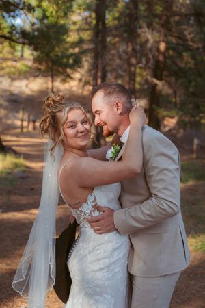 A romantic wedding portrait of a couple embracing in a sun-dappled forest setting.