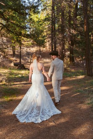 A couple walks along a forest path with the bride wearing a stunning lace-trimmed mermaid wedding dress.