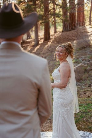 A romantic outdoor wedding moment with a bride in a flowing white dress and veil amidst tall pine trees.
