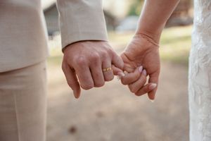 Close-up shot of two people holding pinky fingers together in a promise gesture against a blurred outdoor background.
