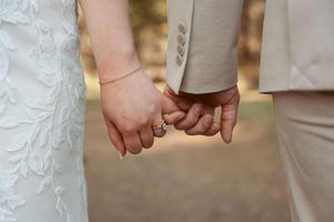 Close-up of newlyweds holding hands showing wedding attire details.