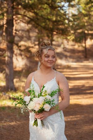 Outdoor bridal portrait featuring a white lace dress and elegant bouquet in a wooded setting.