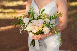 Close-up of a delicate bridal bouquet with white roses and greenery against a lace wedding dress.