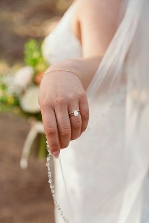 Close-up detail of a bride's hand with engagement ring holding white lace wedding dress.