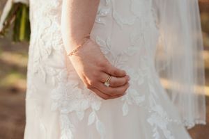 Close up detail of intricate lace wedding dress and delicate bracelet on bride's hand.