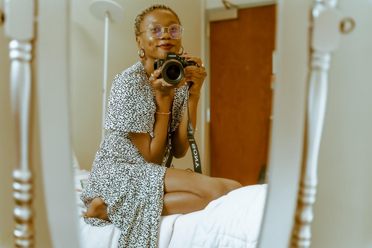 A photographer takes a self-portrait in a mirror while holding a camera and wearing a polka dot dress.