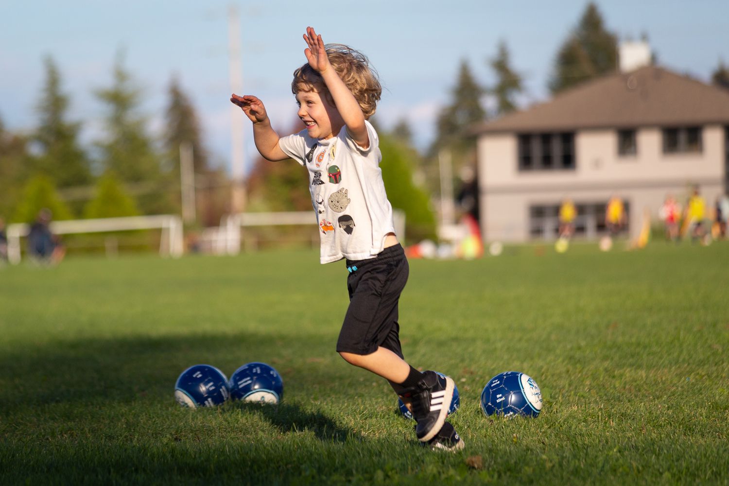 Youth soccer player leaping joyfully on a grass field with blue cleats in the background.