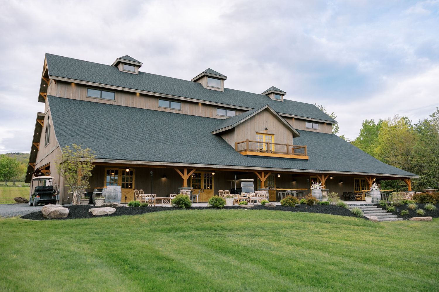 Windham Manor, a large wooden barn-style event venue with green roof and stone pillars sits on a manicured lawn under cloudy skies.