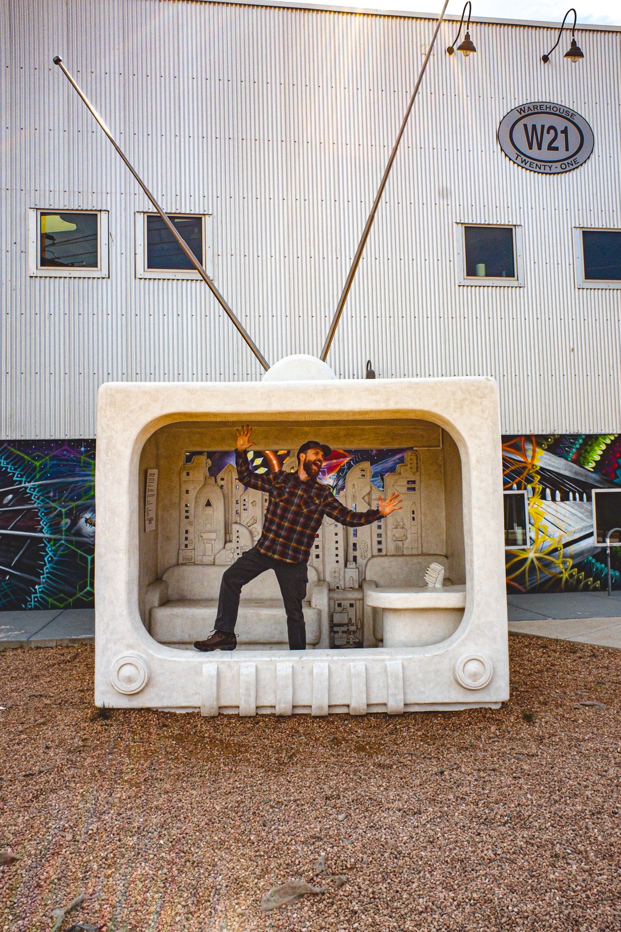 Giant TV sculpture with antenna and a man, Alex Kent in plaid shirt pretending to be stuck inside pressing up against the non-existent glass
