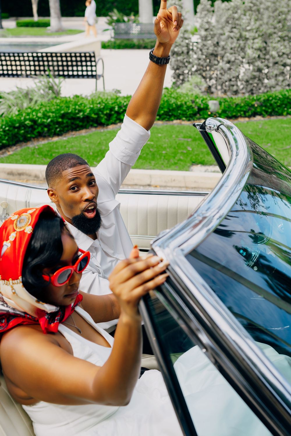 Joyful couple raising hands and celebrating while sitting in red convertible car.