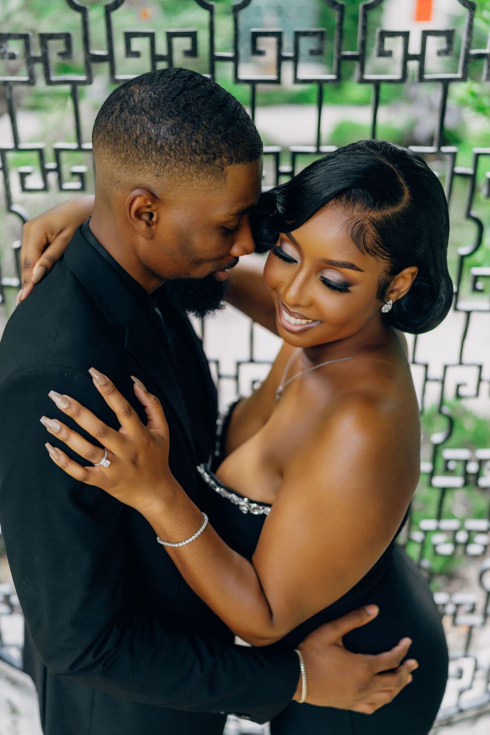 A romantic couple embraces against a decorative wall with geometric patterns while sharing an intimate moment in formal attire.