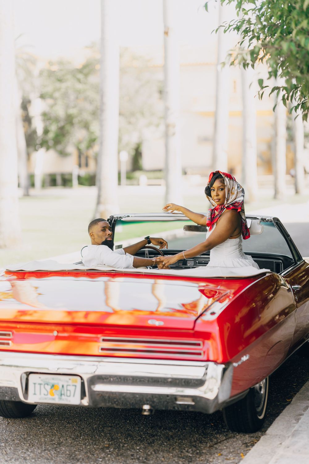 A classic red convertible car parked on a sunny day with palm trees in the background.