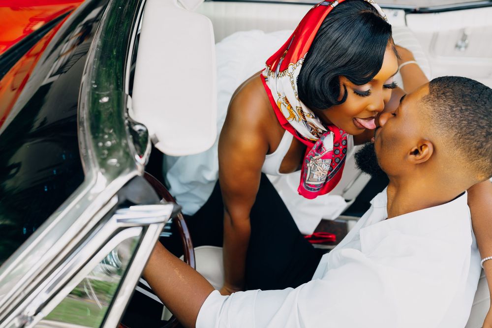 A romantic couple shares an intimate moment while leaning into a classic car with red accents.