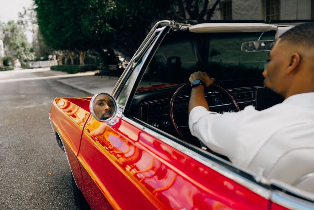 A person driving a vintage red convertible car parked on a city street.