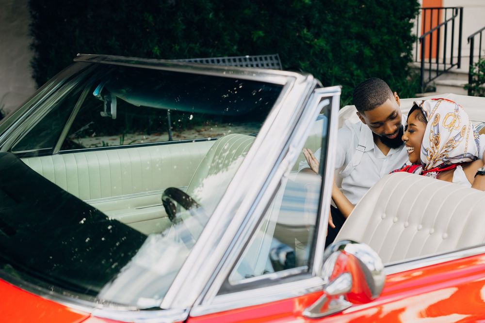 People sit in a vintage red and white classic car on a sunny day.