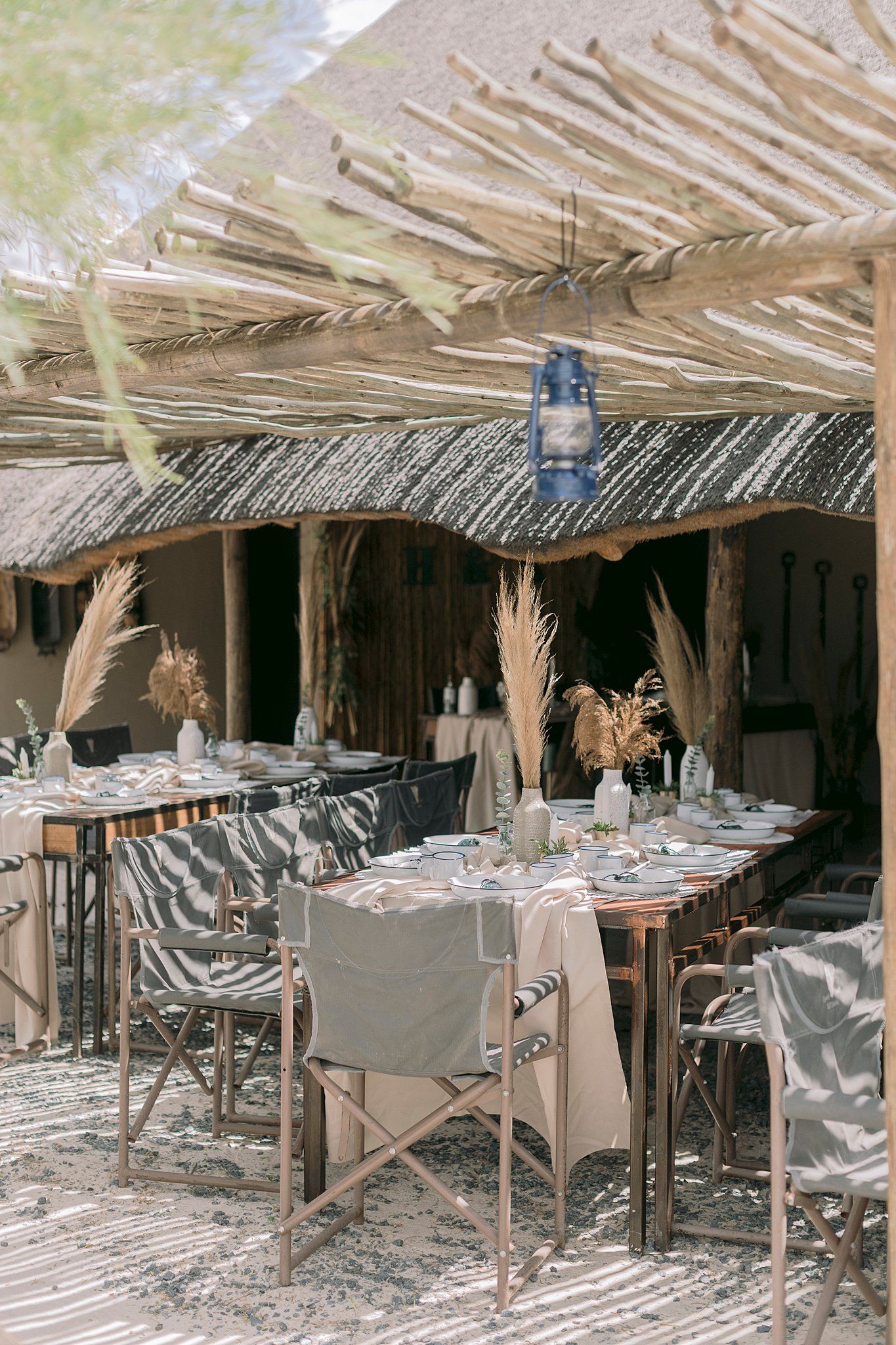 Safari-style outdoor wedding reception venue with thatched roof, wooden tables, and boho decor.
