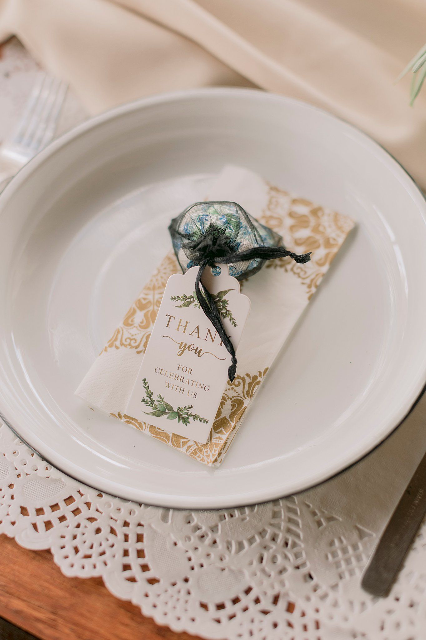 Close-up of a wedding favor thank you tag on a white plate with a lace placemat at a reception.
