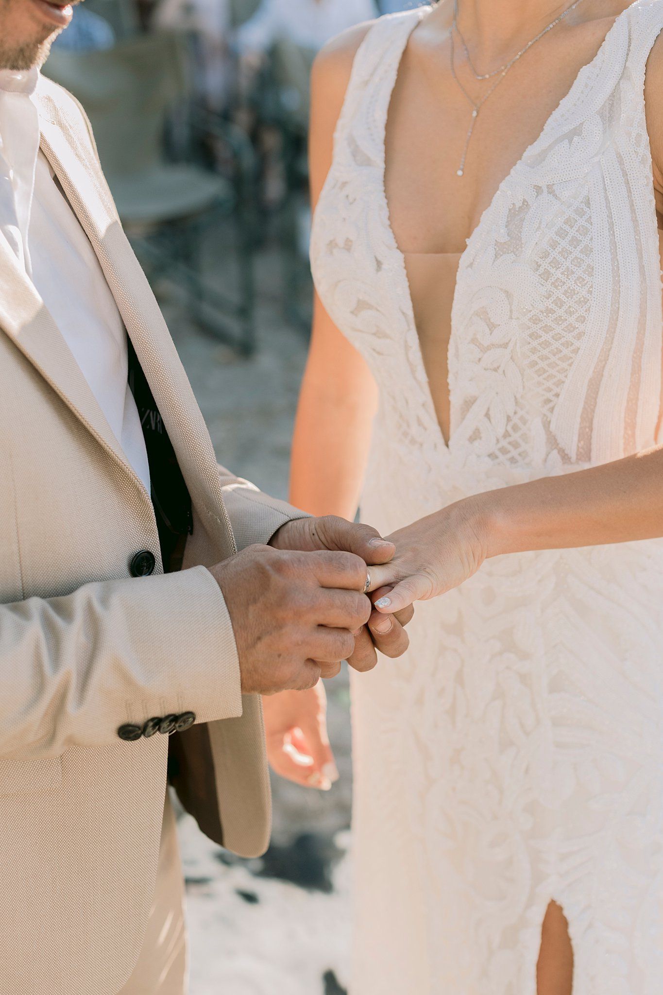 Close-up of bride and groom holding hands during outdoor wedding ceremony in warm sunlight.