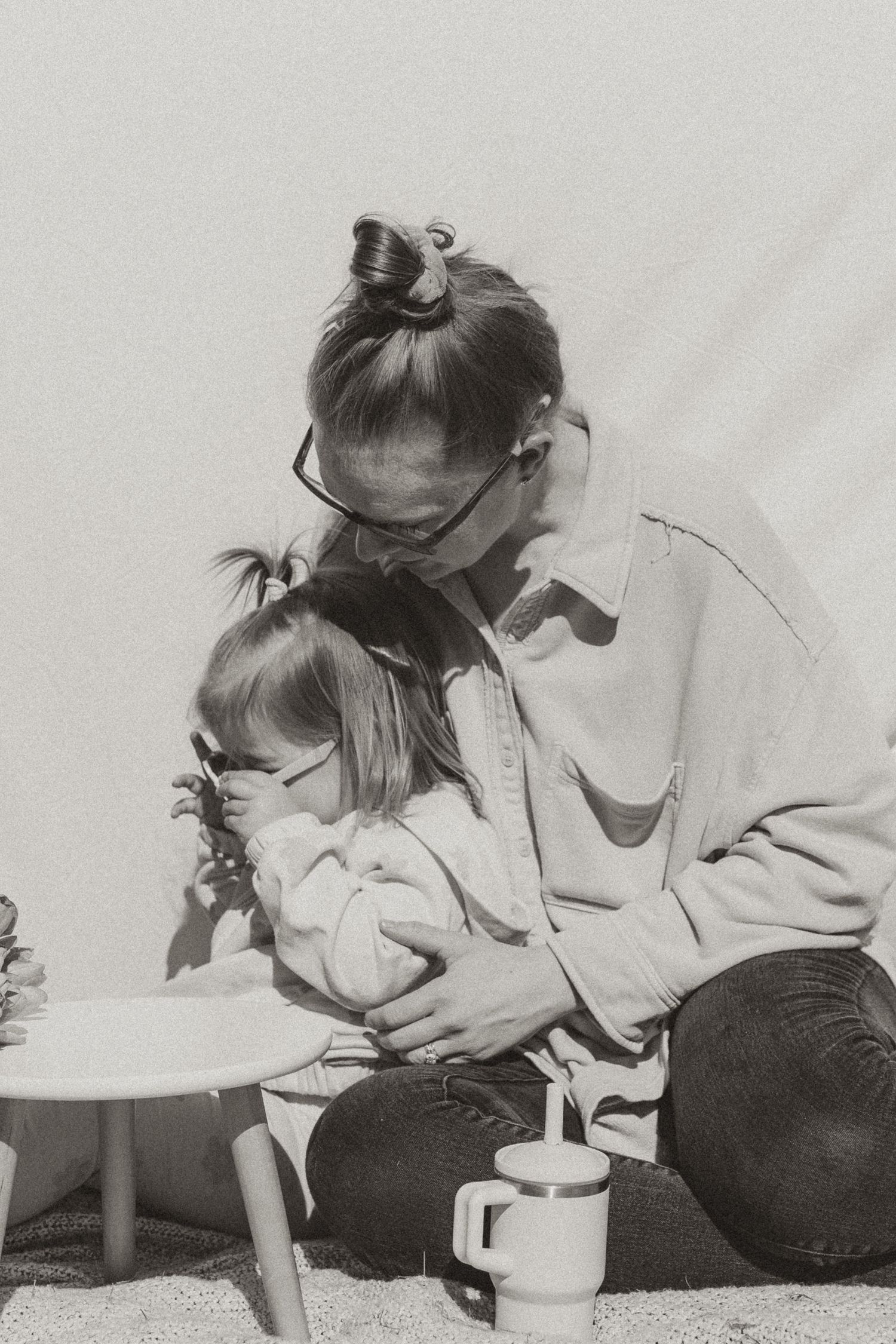 A tender black and white photograph shows an intimate parent and child moment in casual dress with a coffee mug nearby.
