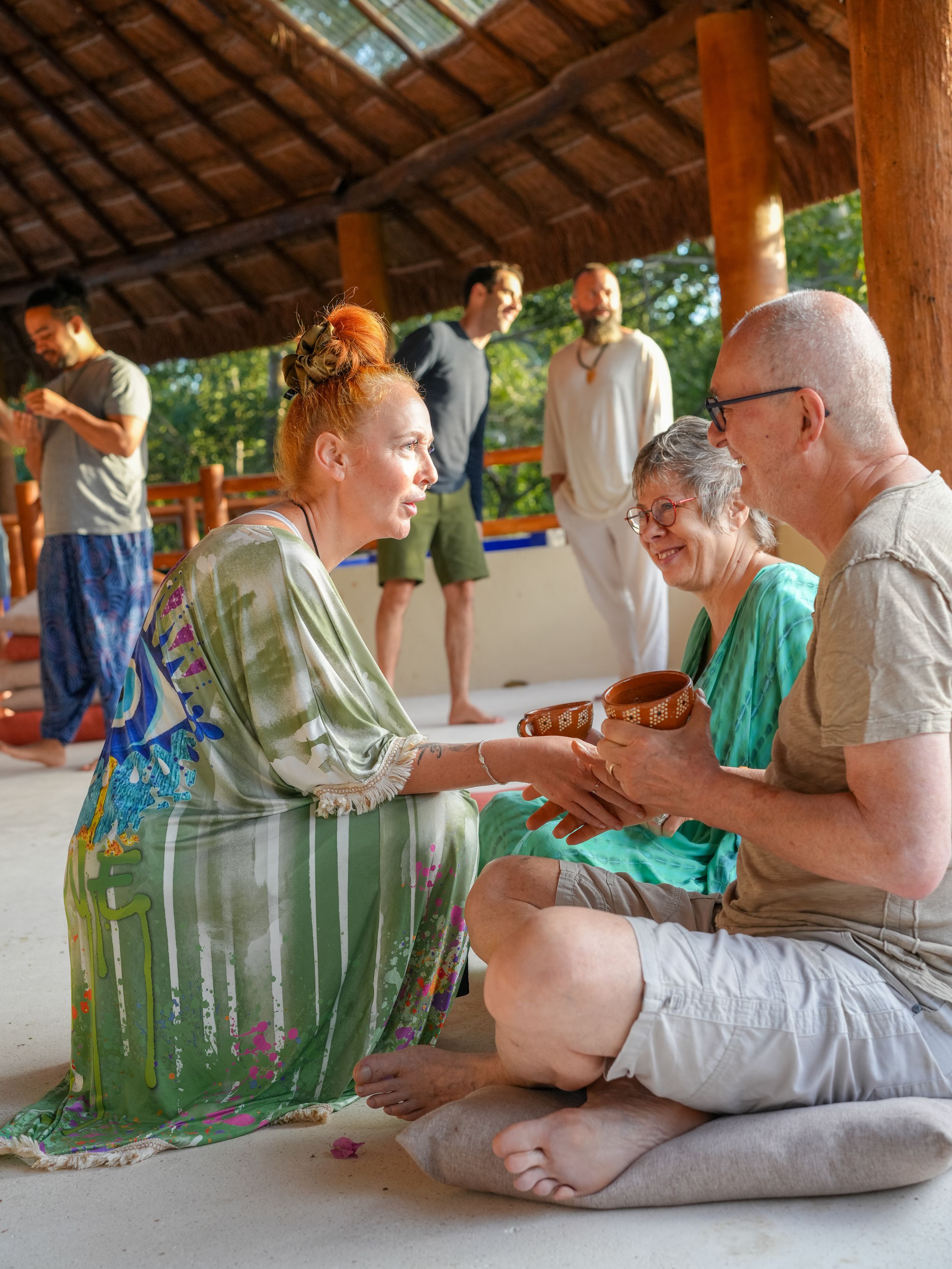 People sharing a quiet moment during a wellness retreat under a thatched roof structure.
