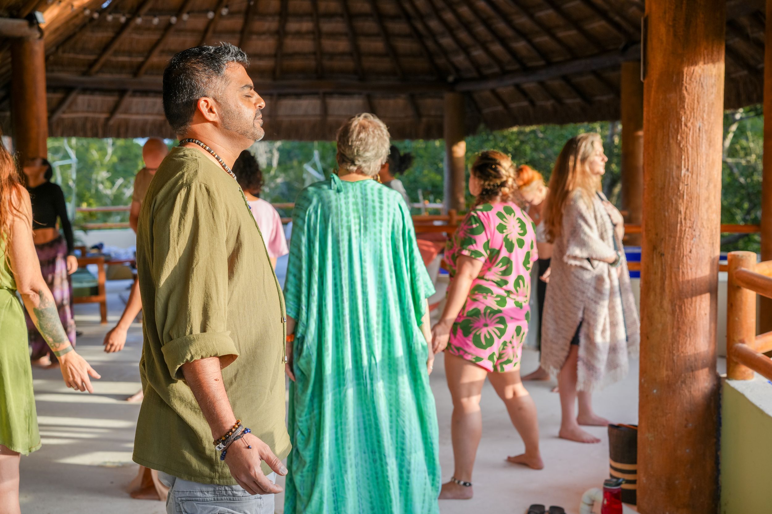 People participating in movement exercises under a covered outdoor space with wooden posts.