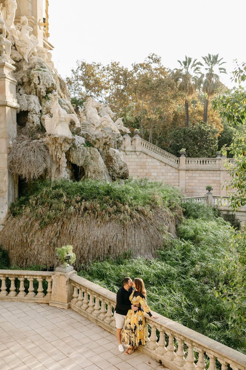 Romantic photoshoot along stone balustrade with lush garden backdrop.