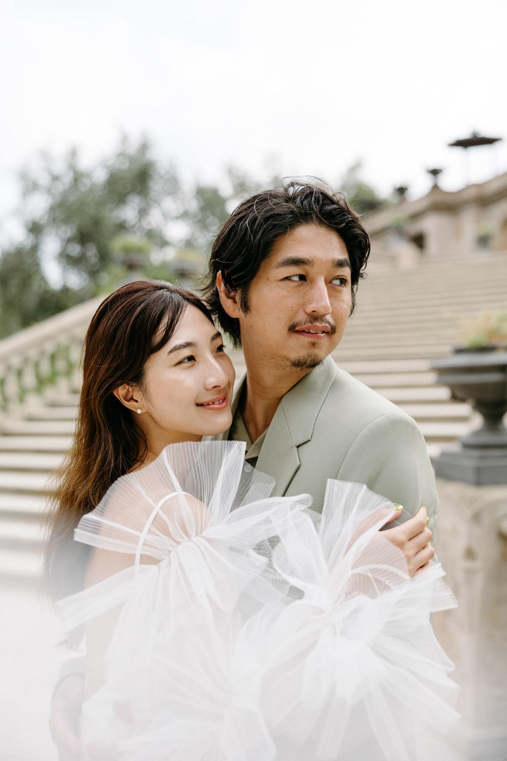 Elegant couple with white fan poses on historic stone steps.