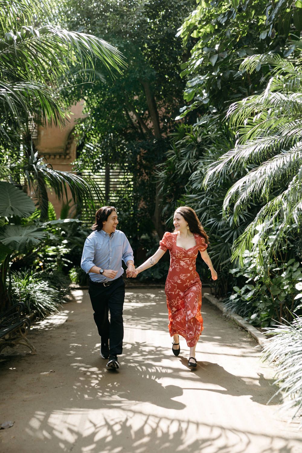 Couple walks hand in hand through lush tropical garden path with dappled sunlight.