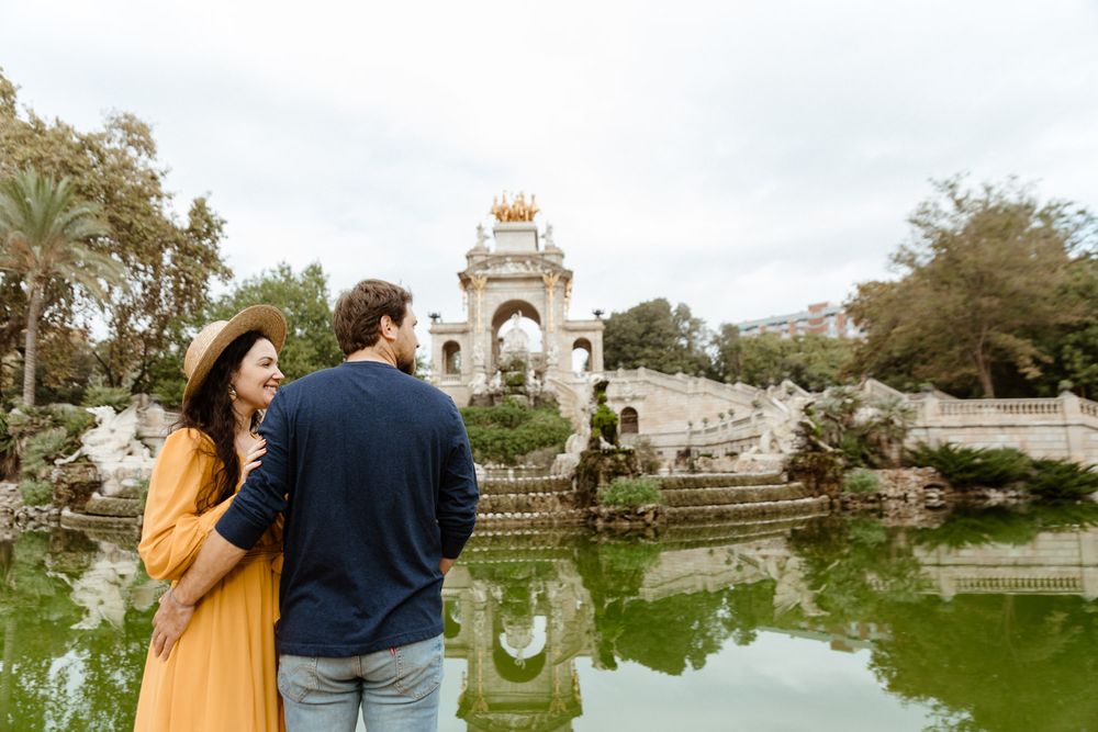 Romantic couple walks along grand stone architecture overlooking scenic pond.