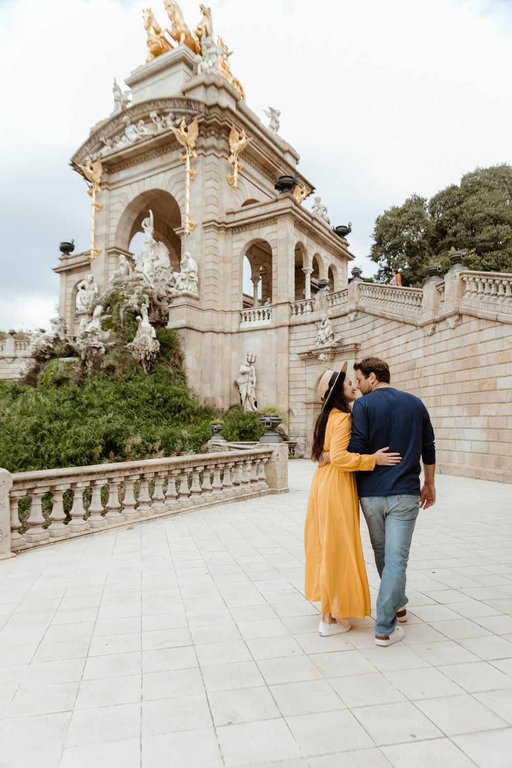 Couple walks along stone pathway with grand classical architecture and columns in background.