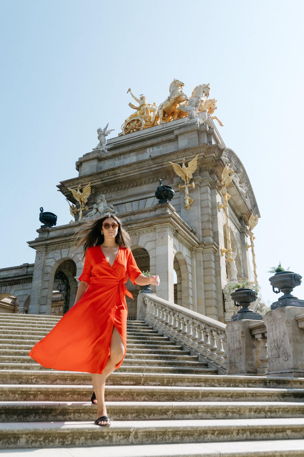 Woman in flowing red dress dances on stone steps of classical building with ornate architecture.