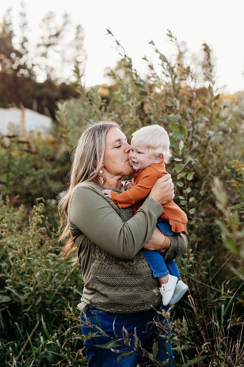 A tender moment captured outdoors in natural lighting among greenery during golden hour.