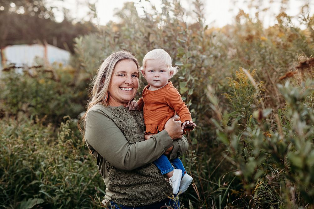 Parent and child share a joyful moment together outdoors among greenery at sunset.